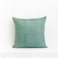 a green and white pillow sitting on top of a white bed cover covered in polka dots