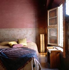 a bed in a room with red walls and wooden furniture next to a large window