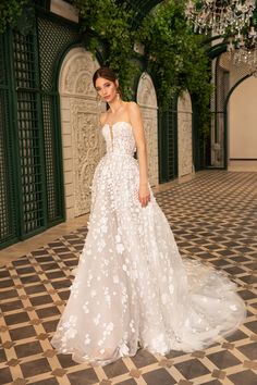 a woman in a white wedding dress standing on a tiled floor with greenery behind her