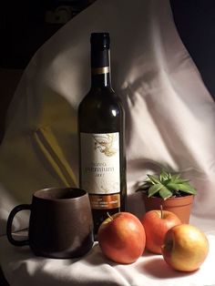 a bottle of wine sitting next to some fruit and a cup on a white cloth