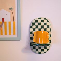 a yellow cup is sitting on a black and white checkerboard wall shelf next to a painting