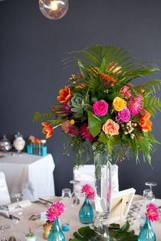 a vase filled with lots of colorful flowers on top of a white table cloth covered table