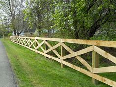 a long wooden fence on the side of a road in front of trees and grass