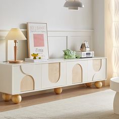 a white entertainment center in a living room with wooden legs and an art piece on top