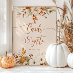 a card and gifts sign sitting on top of a table next to white pumpkins