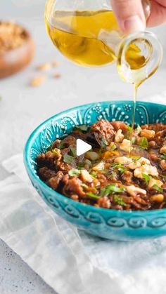 someone pouring olive oil into a bowl filled with chili and beans, on top of a white napkin