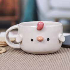 a cup with a chicken face on it sitting next to crackers and a cell phone