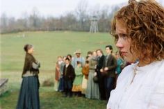 a woman standing in front of a group of people on a lush green field next to a forest