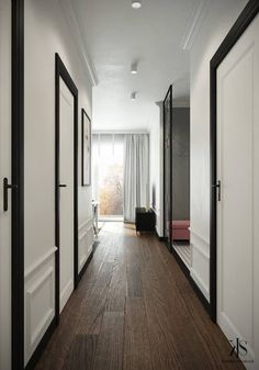 an empty hallway with white walls and black trim on the doors, wood flooring