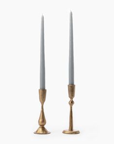 two gold candlesticks sitting next to each other on a white surface with one candle in the middle