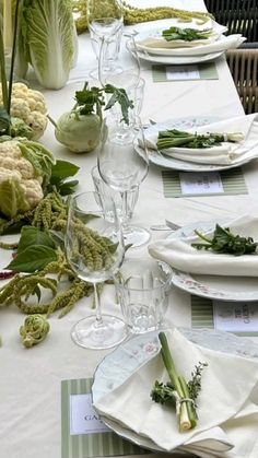 the table is set with white plates, green napkins and flowers in vases