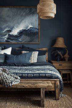 a bed with blue sheets and pillows in a room next to a painting on the wall