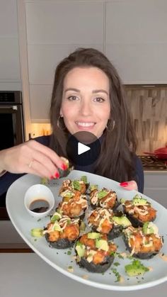 a woman holding a plate with sushi on it and dipping sauce in front of her