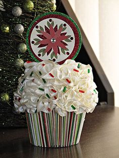 a cupcake decorated with white frosting on top of a table next to a christmas tree