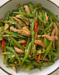 a white bowl filled with green beans and meat