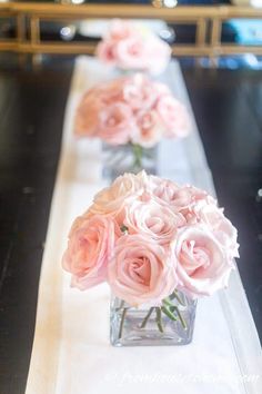 three vases filled with pink roses sitting on a long white table cloth lined up