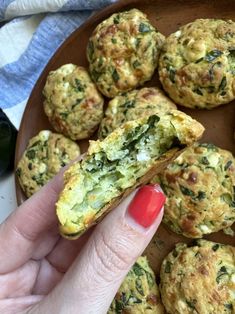 a person is holding a muffin with spinach and cheese on it in front of other muffins