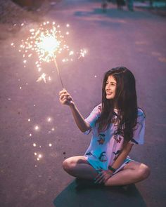 a woman sitting on the ground holding a sparkler