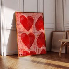 a painting with red hearts on it sitting in front of a wooden chair and wall