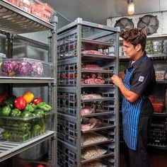 a man standing in front of an open refrigerator filled with lots of vegetables and meat