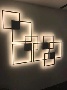 a white wall with square and rectangle shapes lit up by light coming from the ceiling