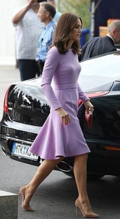 a woman in a purple dress walking next to a car