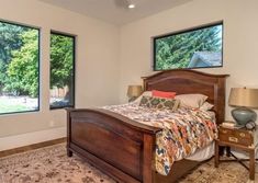 a bed room with a neatly made bed next to two windows and a rug on the floor