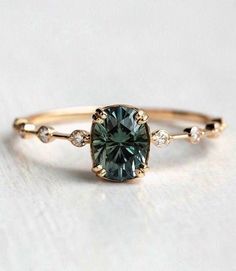 a gold ring with a green diamond and two white diamonds on the band, sitting on a