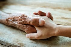 an older person holding the hand of a younger person on a wooden table in front of them