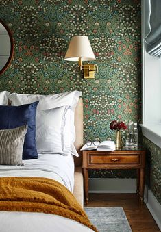 a bedroom with floral wallpaper and gold accents on the headboard, bedside table and mirror