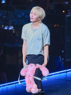 a man holding a pink teddy bear on top of a stage with blue lights behind him