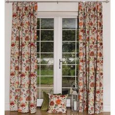 an open window with floral curtains and pillows on the floor next to it, in front of a white door