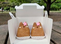 two cupcakes in the shape of animals with pink bows on their heads are sitting in a cardboard box