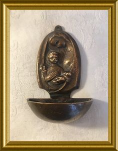 a gold frame holding a bronze sculpture of a baby in a bowl on a white wall