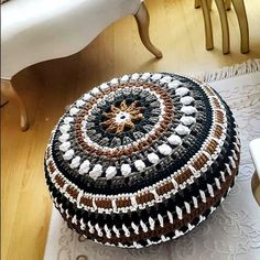 a crocheted round ottoman sitting on top of a wooden floor next to a white table