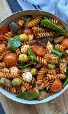 a bowl filled with pasta and vegetables on top of a wooden table