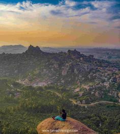 a person sitting on top of a rock looking out over the valley and mountains at sunset