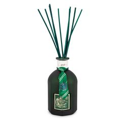 a bottle filled with green reeds sitting on top of a white table next to a candle