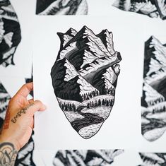 a person holding up a piece of paper with mountains and trees on it in front of black and white background