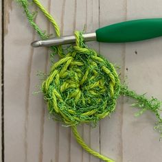 a crochet hook with green yarn on it next to a pair of scissors