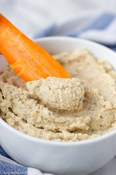 a white bowl filled with hummus and an orange carrot sticking out of the top