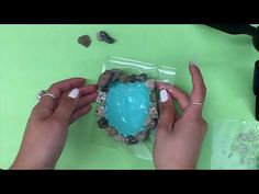 a woman is decorating an egg with blue frosting and rocks on the side