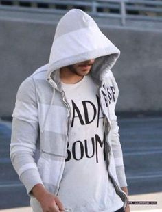 a man in a white hoodie is walking down the street with his hand on his hip