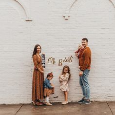 a family poses in front of a white brick wall with the words oh baby written on it