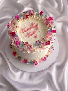 a birthday cake with white frosting and pink flowers on top, sitting on a white cloth