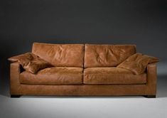 a brown leather couch sitting on top of a white floor next to a black wall