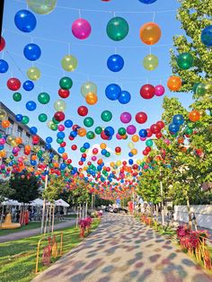 many balloons are floating in the air above a street lined with trees and lawns