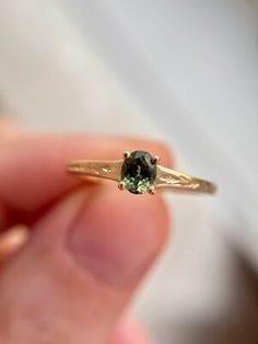 a person holding a ring with a green stone in it's middle and gold band