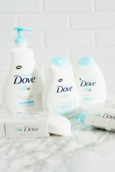 three bottles of dove products sitting on a marble counter top next to two soap bars