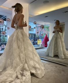 a woman standing in front of a mirror wearing a wedding dress with an open back